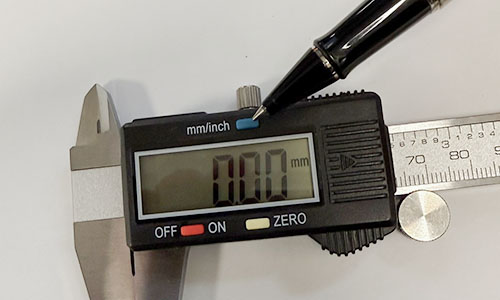 Finger pointing to the inch/millimeter toggle button on a digital caliper