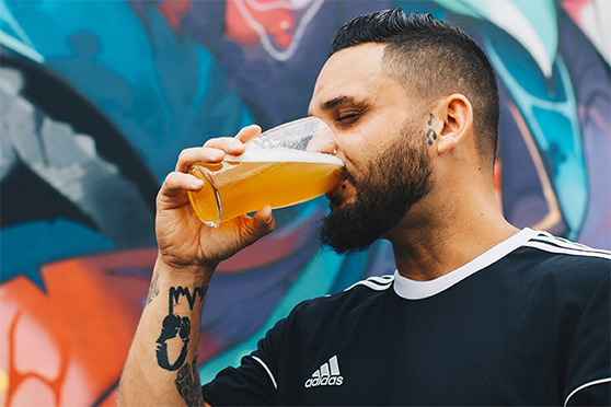 man met een baard die bier drinkt voor een muur met kleurrijke graffiti